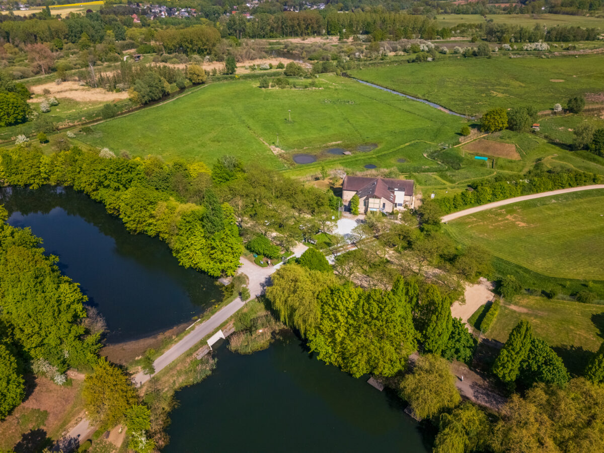Luchtfoto van het Bezoekerscentrum Webbekoms Broek in Diest, omgeven door groene velden en de demonstratietuin